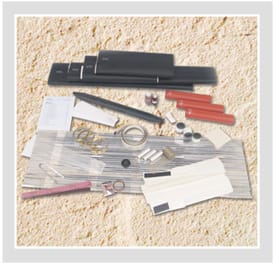 A PILC joint kit unpacked and laid out: a long black wraparound joint case, two red heat-shrink tubes, coiled mesh tape and binding wire, constant force springs and worm drive clips, small ferrules and flat strips of tape and emery.